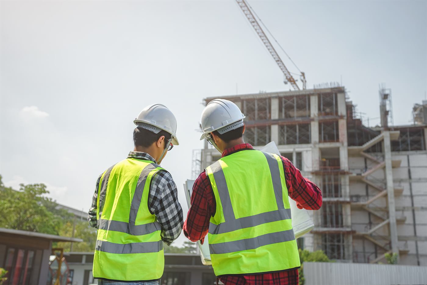 Two engineers in hard hats reviewing plans at a construction site with a tower crane