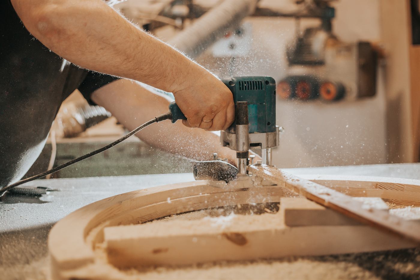 Craftsman routing a curved wooden component in a furniture workshop