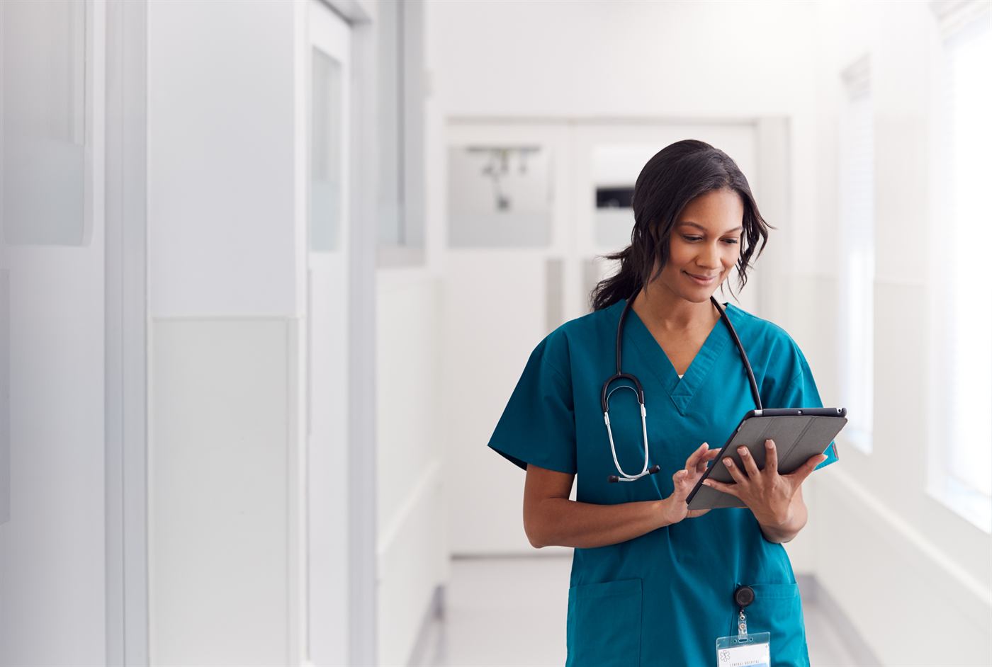 Doctor in scrubs reviewing patient data on a tablet in a hospital corridor