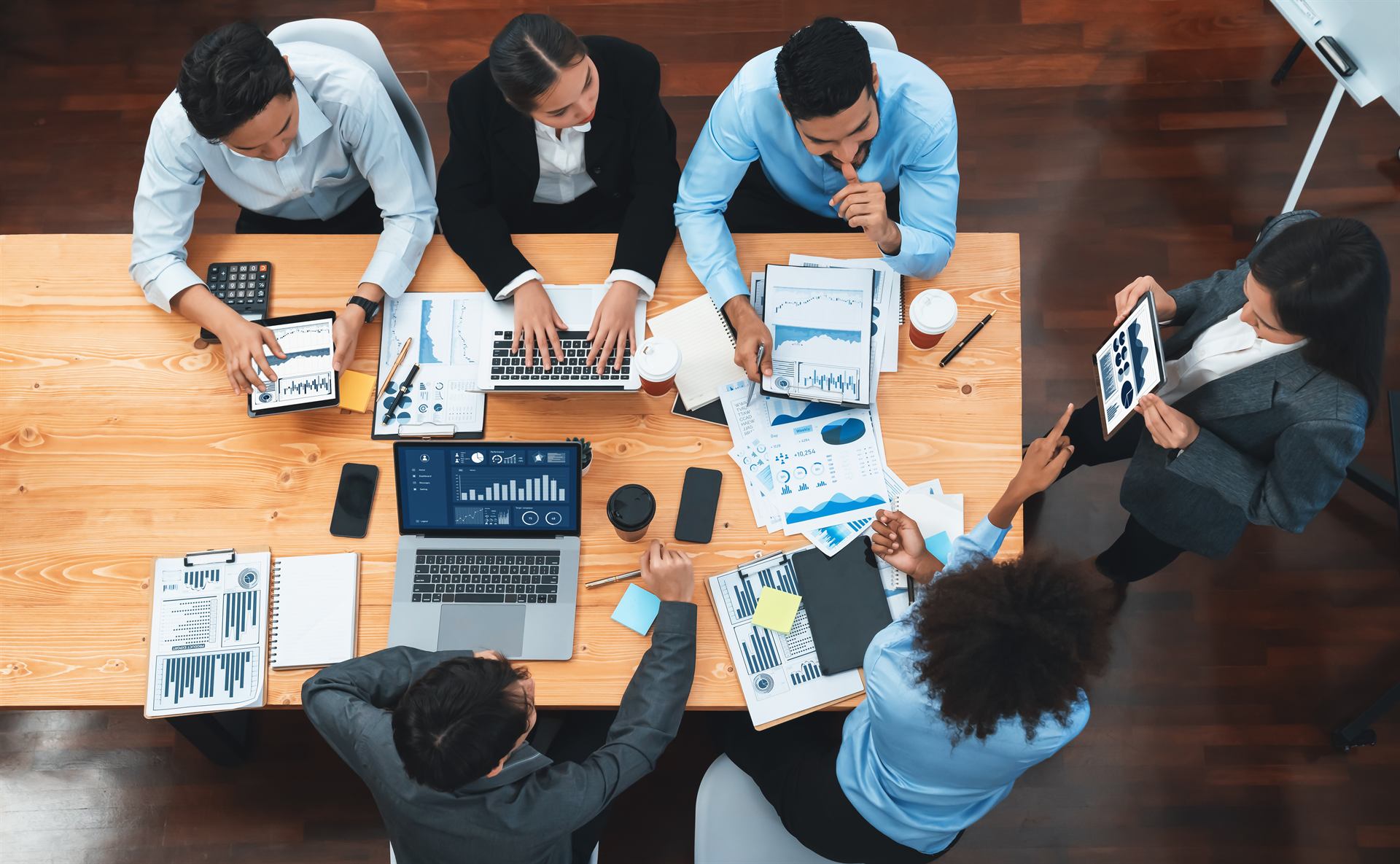 Team reviewing live dashboards and printed reports around a meeting table