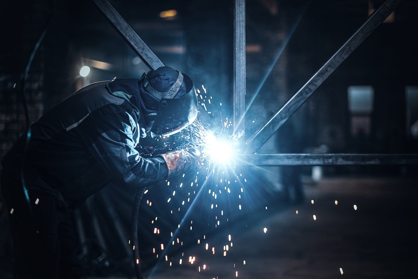 Welder working on a steel structure with sparks in a fabrication shop
